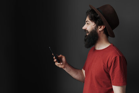 Stylish man in hat using smartphone on moody background
