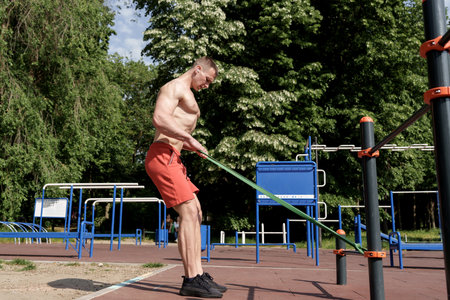 Muscular man doing resistance band training outdoors