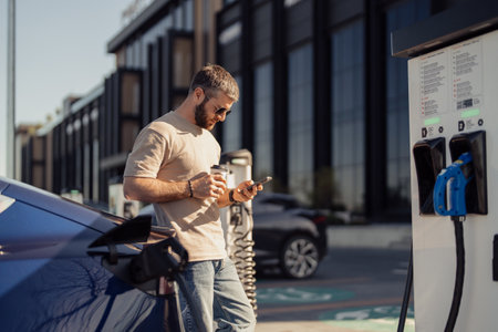 Man using smartphone while charging electric carの写真素材