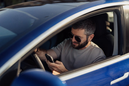 Man using smartphone in electric car on sunny day