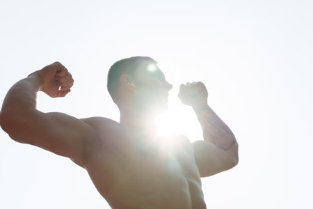 Strong athlete flexing muscles with sun flare