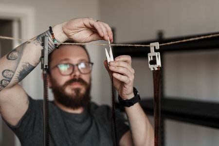 Bearded man hanging film negatives with clothespins at home