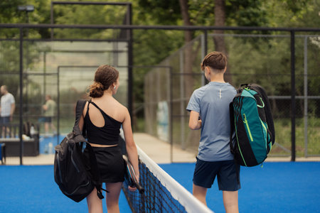 Kids walking on a padel tennis court with sports bagsの写真素材