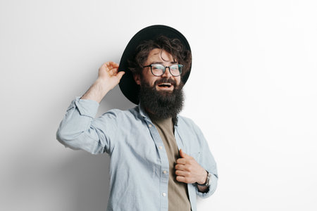 Joyful bearded man tipping hat and smiling against white background