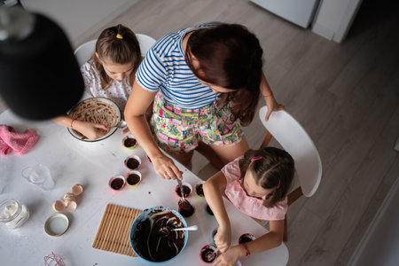Mother and daughters baking cupcakes together at home in kitchenの写真素材