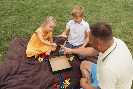 Father playing board game with children at outdoor picnic in park