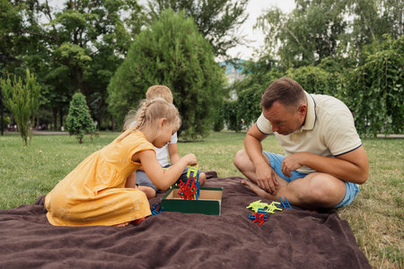 Father and children playing in park with toy blocks on blanket