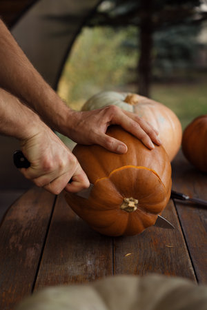 Hands carving a pumpkin on a wooden table outdoorsの写真素材