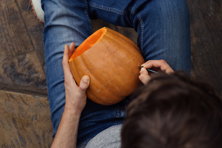 Person carving a Halloween pumpkin with intricate design detailsの写真素材