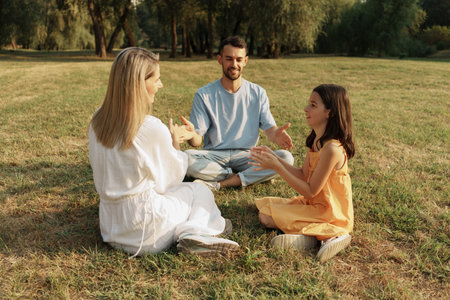 Family enjoying quality time together seated on green grass outdoorsの写真素材