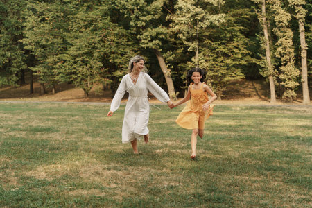Joyful mother and daughter running together in a green parkの写真素材
