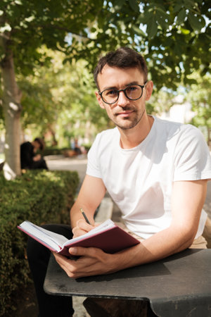 Young man writing in journal while sitting outdoors in parkの写真素材