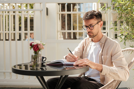 Man writing in notebook at outdoor cafe table with flowersの写真素材