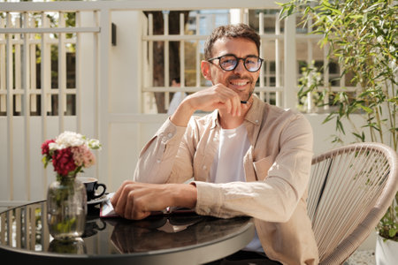 Smiling man enjoying outdoor coffee at a sunny cafeの写真素材