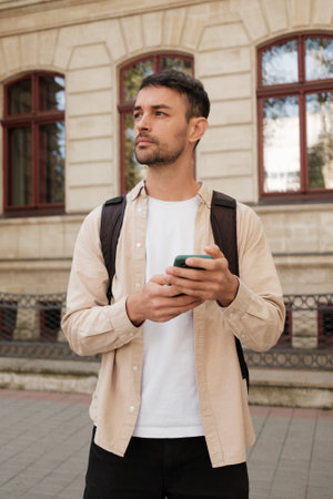 Thoughtful young man with smartphone standing outside historic buildingの写真素材