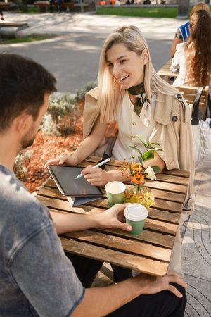 Casual meeting at an outdoor cafe with coffee and tablet discussionの写真素材