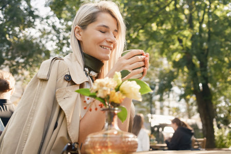 Woman enjoying a warm drink in sunny outdoor cafeの写真素材