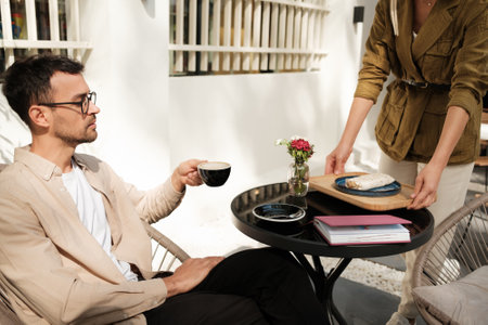 Man enjoying coffee at outdoor cafe with a server bringing foodの写真素材