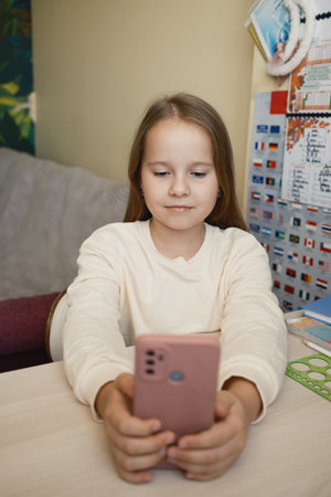 Child using smartphone while seated at a desk with educational materials