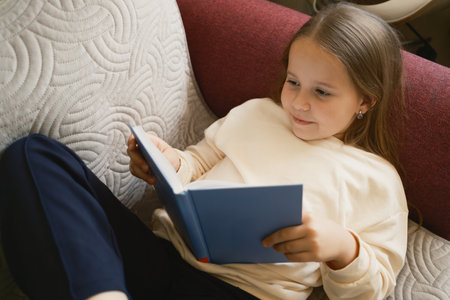 Young girl reading a book while relaxing on a comfortable couch