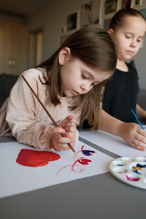 Two Girls Engaged in Creative Art Activities with Paint and Brushesの写真素材