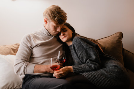 Warm couple embracing on a couch while enjoying drinks togetherの写真素材