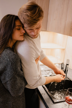 Romantic couple sharing an intimate moment while washing dishes together in a kitchenの写真素材