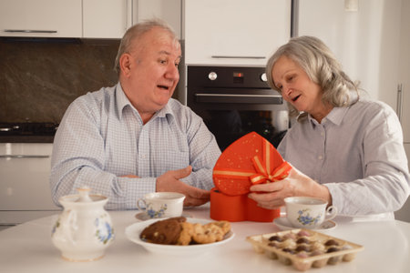 Happy older couple exchanging gifts while enjoying tea in a modern kitchenの写真素材