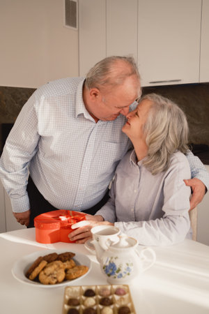 Elderly couple sharing a romantic moment with a gift in their kitchenの写真素材
