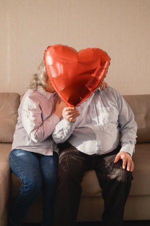 Elderly couple with red heart balloon celebrating love and togethernessの写真素材
