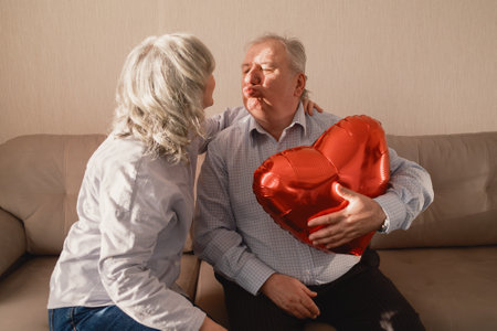 Elderly couple sharing a moment with heart-shaped balloon indoorsの写真素材