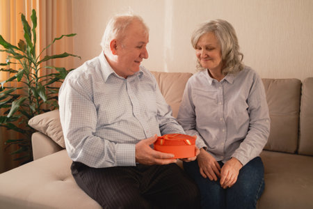 Elderly couple sharing a heartfelt moment with a gift on a couchの写真素材