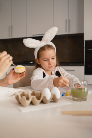 Child painting Easter eggs while wearing bunny ears in a festive kitchenの写真素材