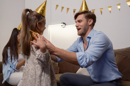 Man and girl celebrating a party with golden hats and decorations indoorsの写真素材