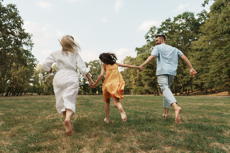 Happy family running together in a sunny green park outdoorsの写真素材