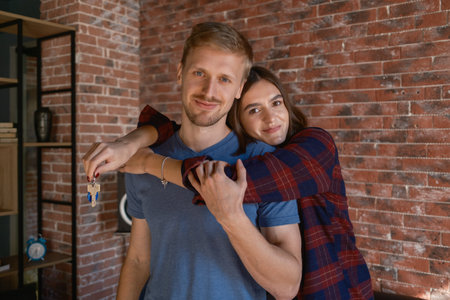 Happy couple holding new house keys at home celebrating their new beginningの写真素材