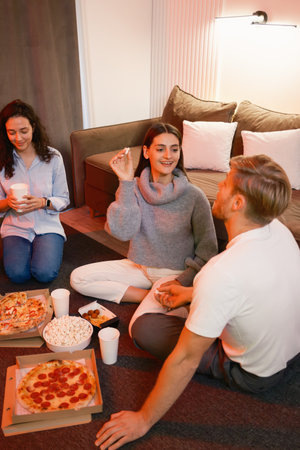 Friends enjoying a casual night with pizza, popcorn, and great conversation at homeの写真素材