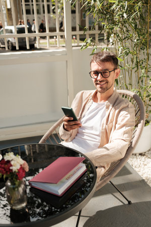 Man enjoying a sunny day outdoors with smartphone and booksの写真素材