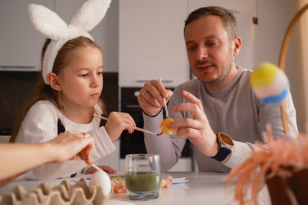 Father and daughter painting Easter eggs together in a cozy kitchenの写真素材