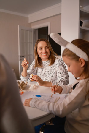 Smiling mother and daughter painting Easter eggs together at homeの写真素材