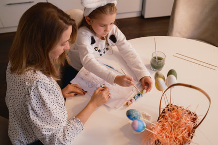 Mother and daughter painting Easter eggs together at a bright indoor tableの写真素材