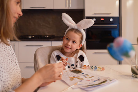 Mother and daughter painting Easter crafts together wearing bunny ears in the kitchenの写真素材