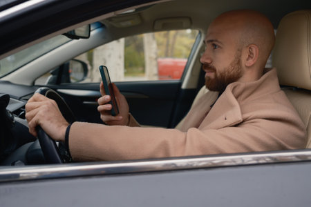 Man driving a car while using a smartphone in an urban settingの写真素材
