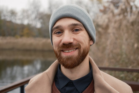 Smiling bearded man outdoors in autumn, wearing a beanie and beige coatの写真素材