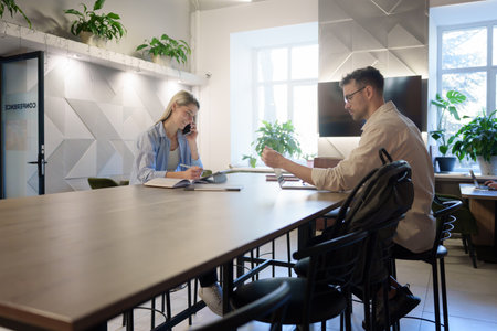 Two coworkers collaborating in a modern office with plants and natural lightingの写真素材
