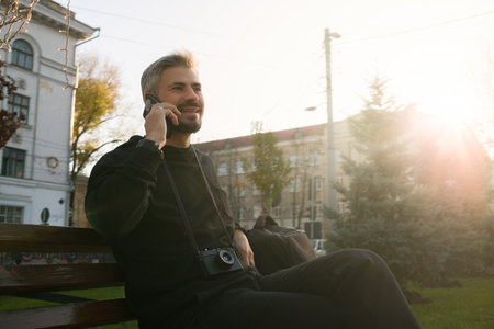 Man sitting outdoors on a bench enjoying a phone call during sunsetの写真素材