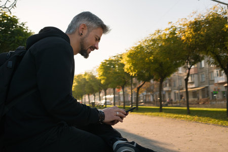 Man sitting outside using a smartphone in a tree-lined street