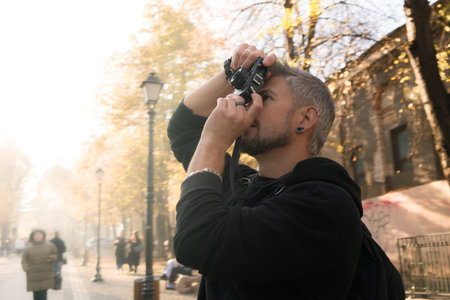 Man taking a photograph in a sunny urban autumn setting