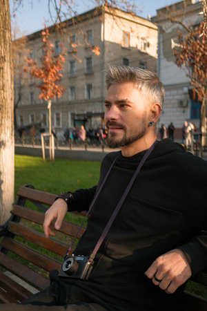 Man sitting on a bench with a vintage camera in a city parkの写真素材