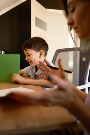 Mother assists young son with his homework at a wooden desk